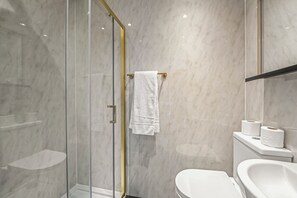 Un baño moderno con cabina de ducha de vidrio, inodoro blanco y lavamanos.