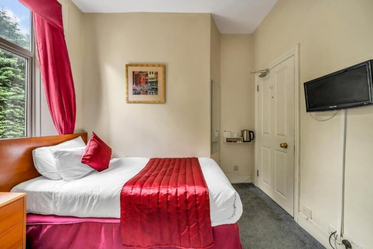 Una habitación de hotel con cama, televisor, puerta y ventana con cortinas.