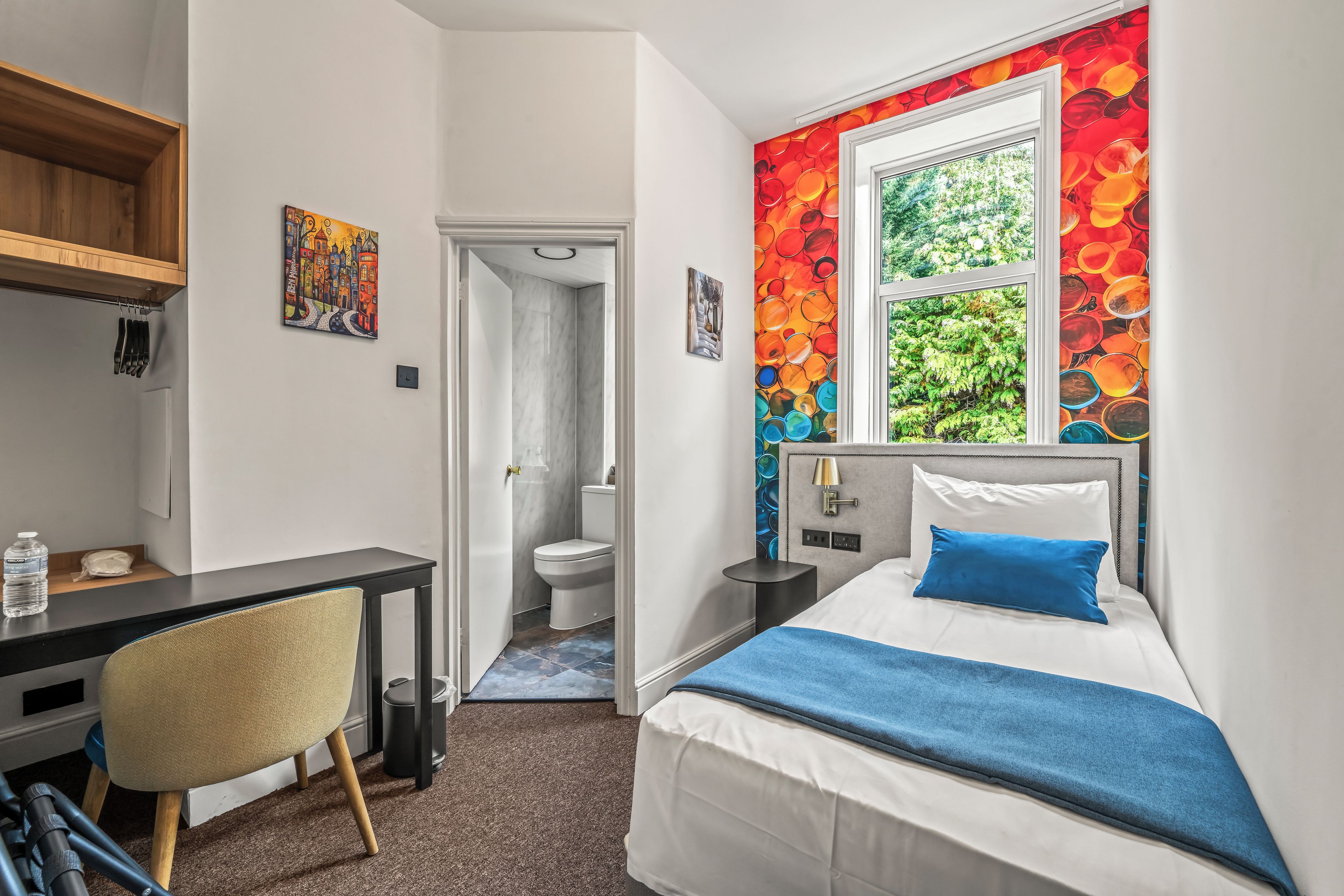 Une chambre d’hôtel équipée d’un lit, d’un bureau, d’une chaise, d’une salle de bain et d’une fenêtre donnant sur un paysage agréable.