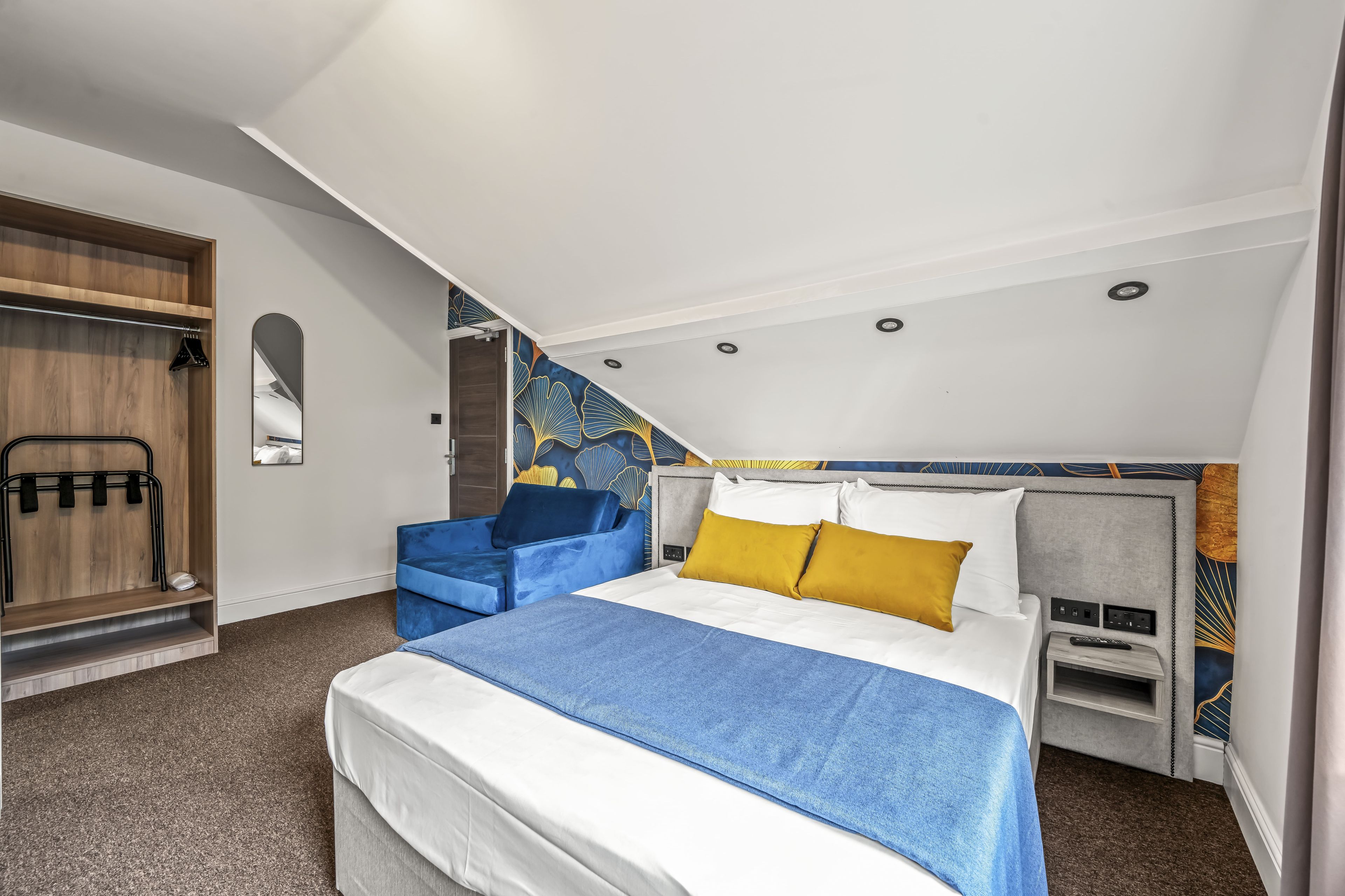A modern hotel room with a bed, a seating area, and a wardrobe.