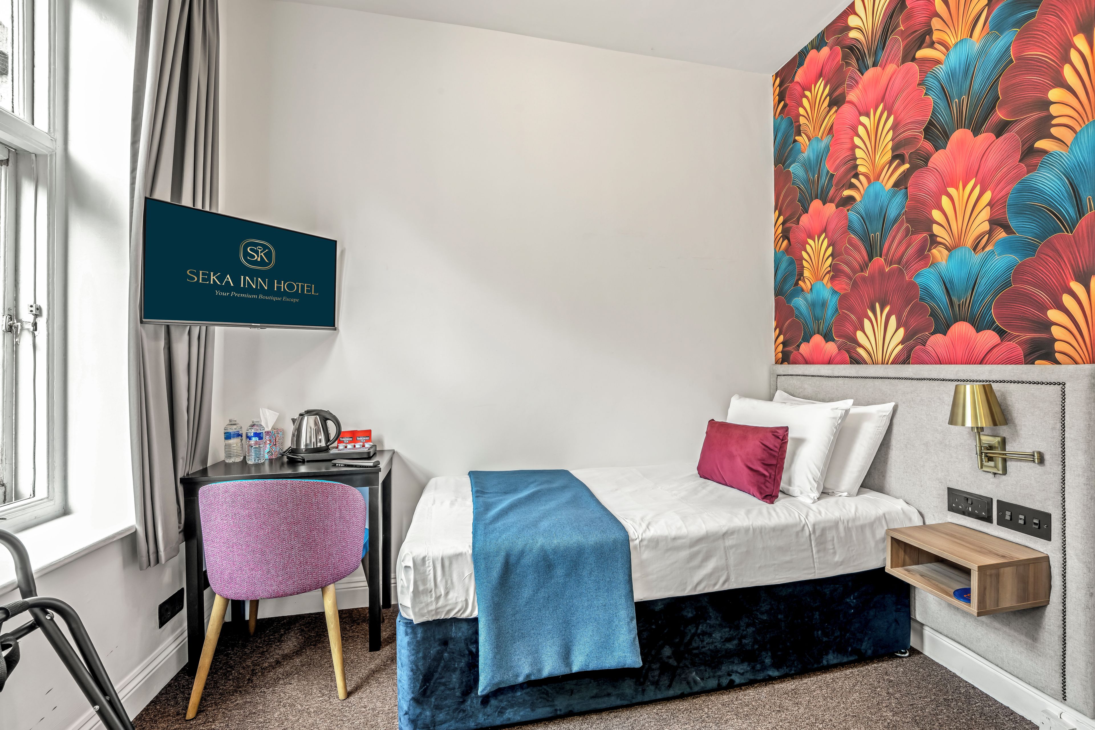 A hotel room with a bed, a desk, a chair, a TV, and a colorful wall mural.