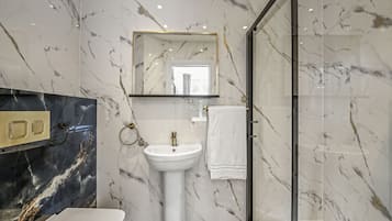 A bathroom with a marble wall, a sink, a mirror, and a glass shower enclosure.