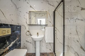 A bathroom with a marble wall, a sink, a mirror, and a glass shower enclosure.