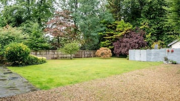 Un jardin avec un chemin de pierres, une pelouse et divers arbres et arbustes.