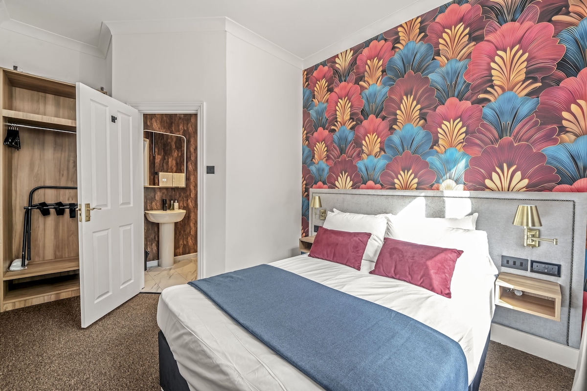 Habitación de hotel con cama, armario, baño y un llamativo papel tapiz floral.