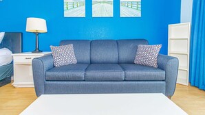 Een kamer met een blauwe bank, twee gestreepte kussens, een witte lamp en drie ingelijste foto's aan de muur.