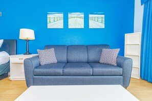 A room with a blue sofa, two patterned pillows, a white lamp, and three framed pictures on the wall. - Sea Mist 51012 Ocean View Escape (Myrtle Beach)