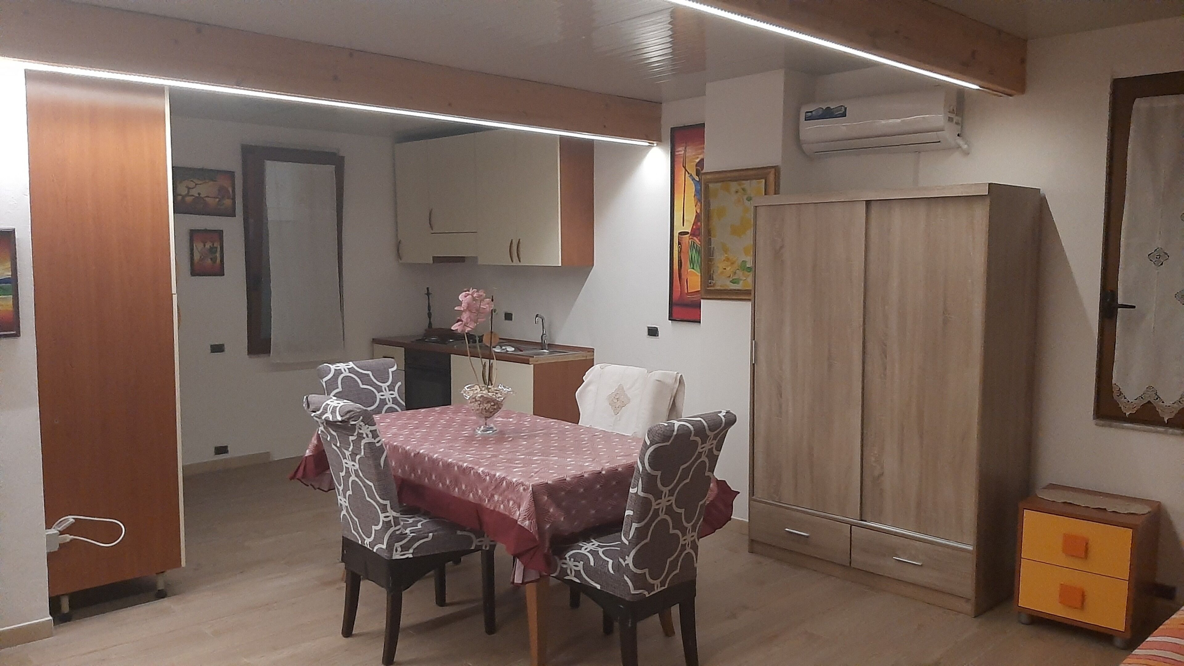 Un ambiente compatto con tavolo da pranzo, due sedie, un armadio e angolo cottura.