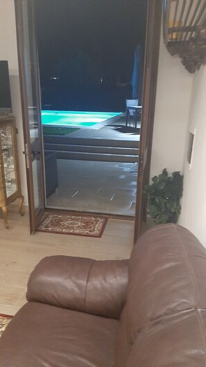 A living room with a brown leather sofa, a glass door leading to a balcony with a pool, and a small table with chairs. - A fully equipped, comfortable, and cozy studio apartment with a pool (Specchia)