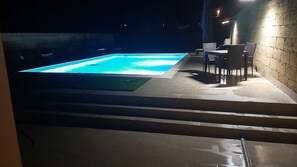Ein Schwimmbecken im Freien mit einer gefliesten Terrasse und einigen Stühlen.