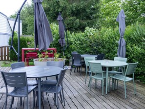 An outdoor patio with round tables and chairs, surrounded by greenery and a wooden deck.