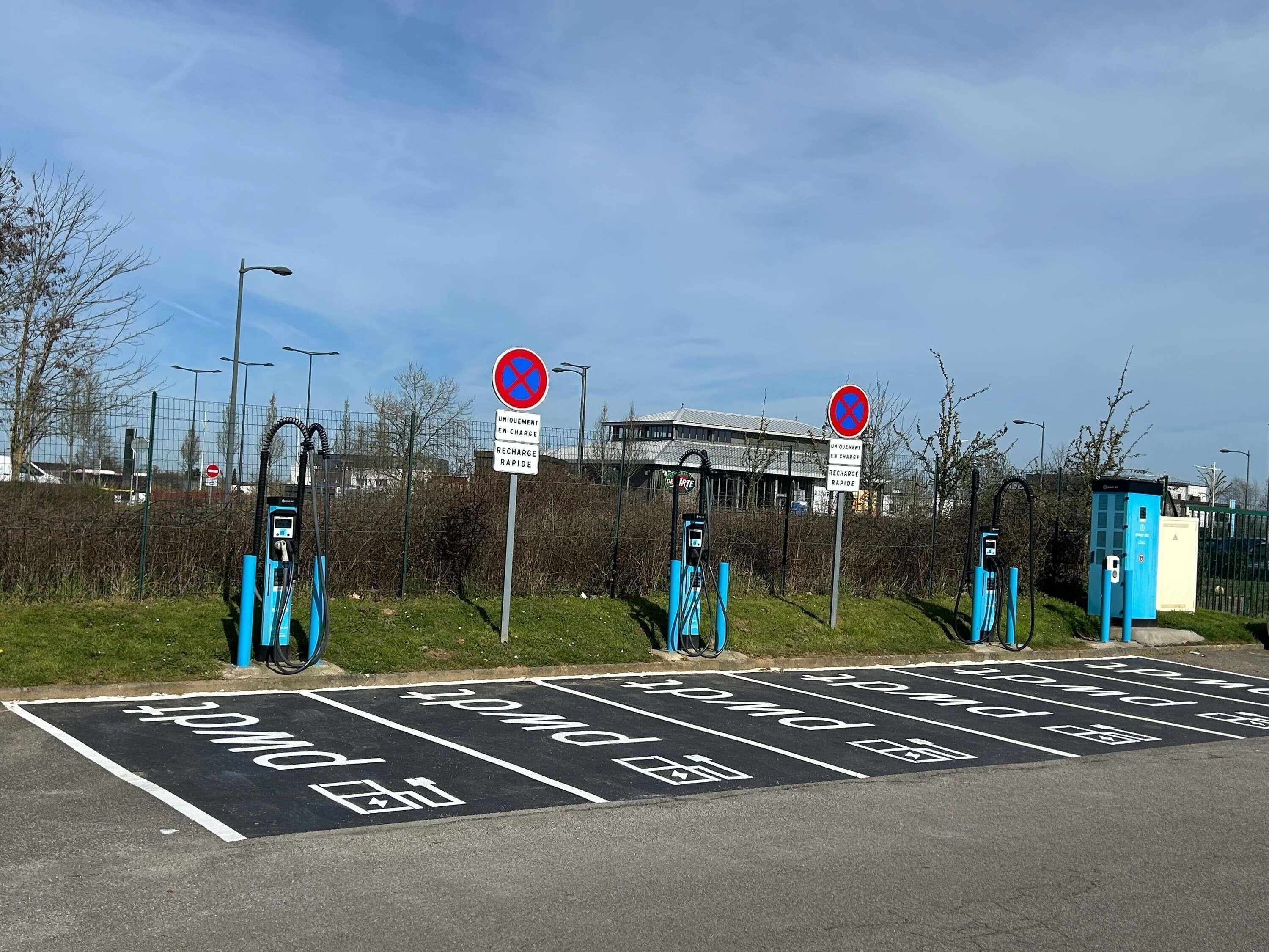 Un espace de stationnement équipé de bornes de recharge pour véhicules électriques, avec un bâtiment en arrière-plan.