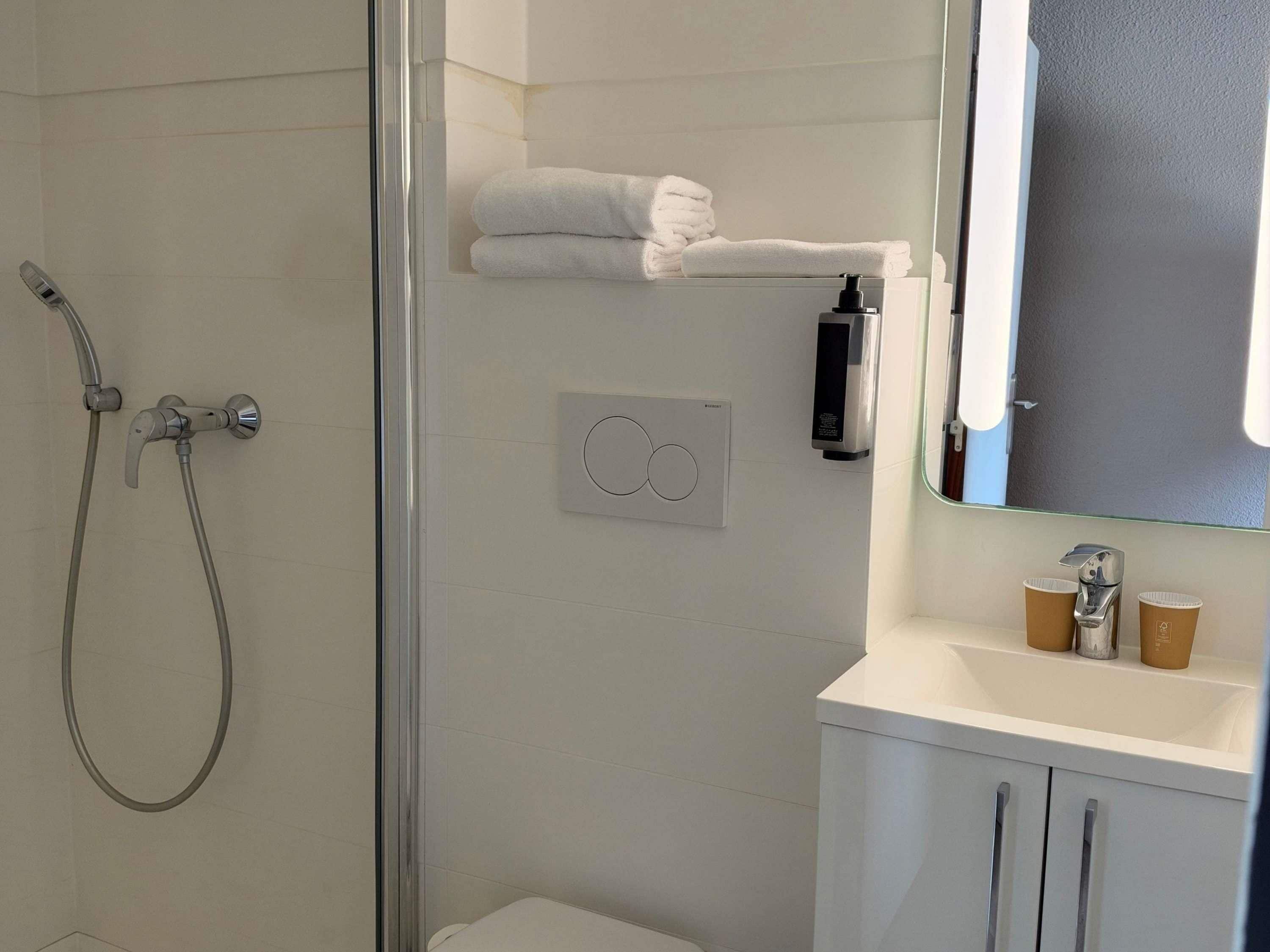 A modern bathroom with a glass shower enclosure, a white sink with a mirror, and a towel rack with folded towels.