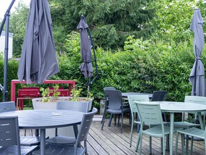 An outdoor patio area with tables and chairs, surrounded by greenery and trees. - Ibis Budget Rouen Nord Isneauville (Isneauville)