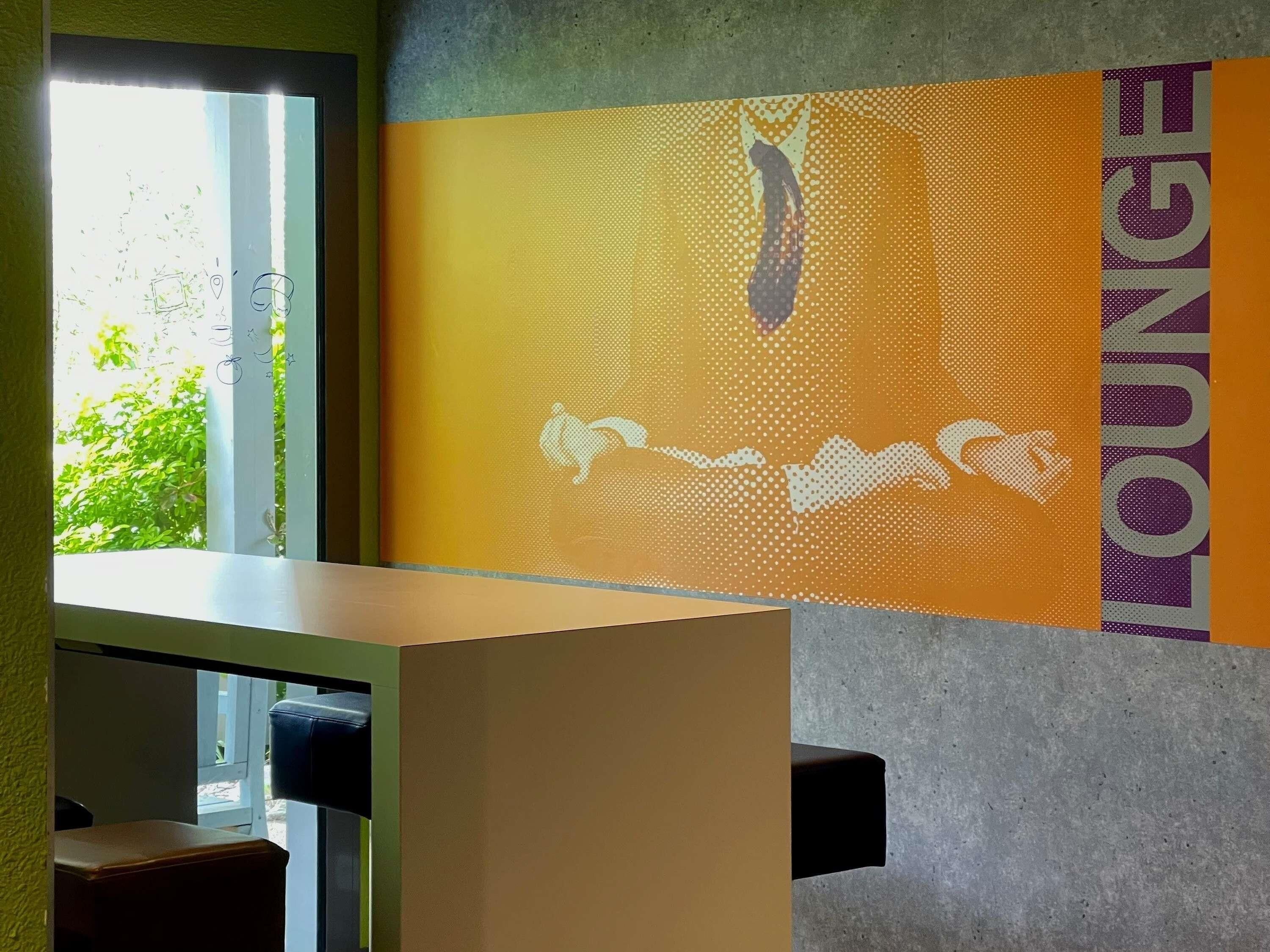 Una habitación con ventanal, pared con diseño gráfico y vista parcial de una cama.