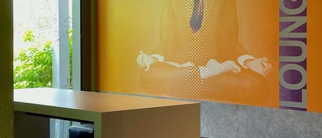 Una habitación con ventanal, pared con diseño gráfico y vista parcial de una cama.