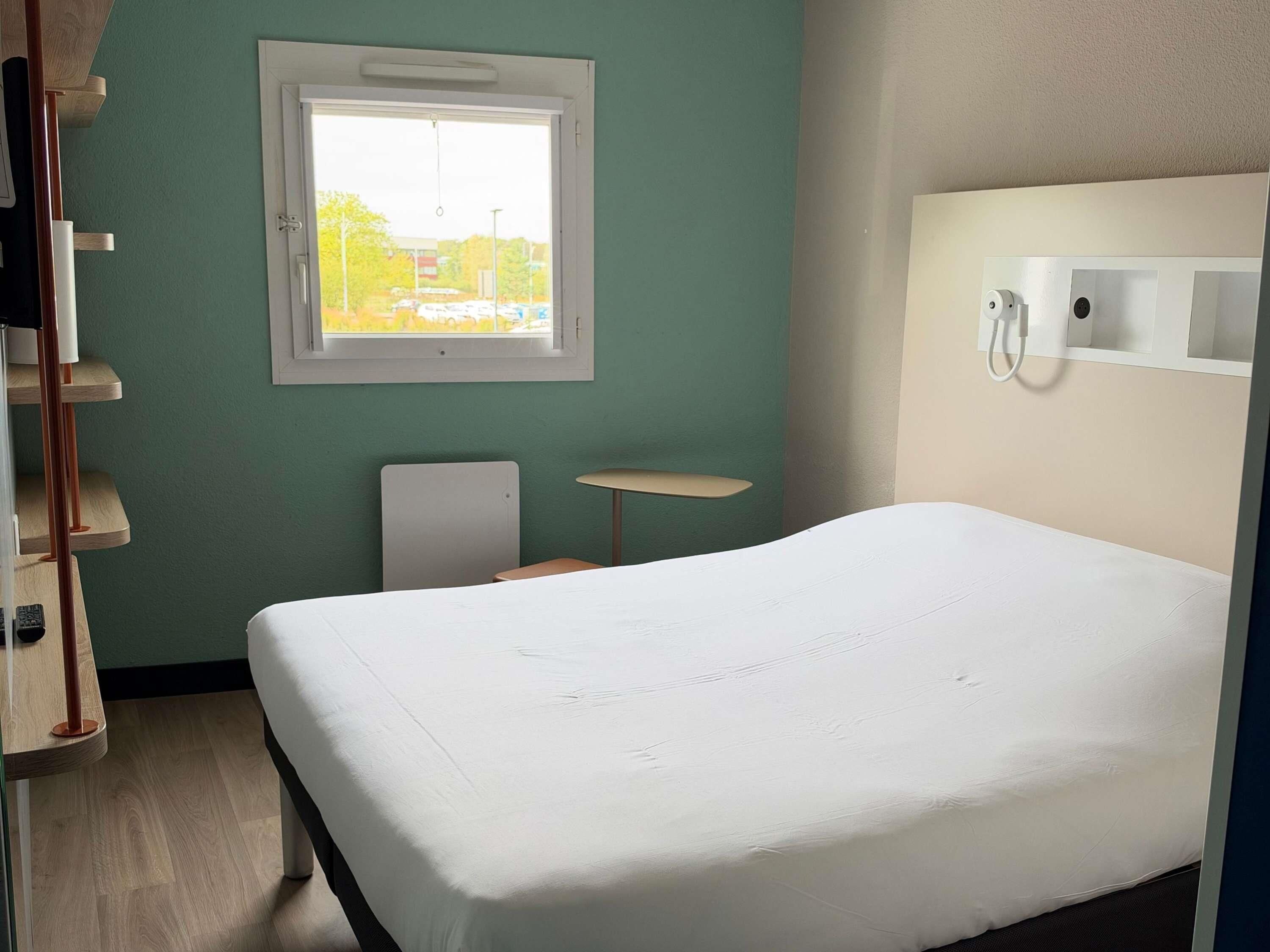 Une chambre d’hôtel comprenant un lit, un bureau, une chaise, une petite table et une fenêtre donnant sur l’extérieur.