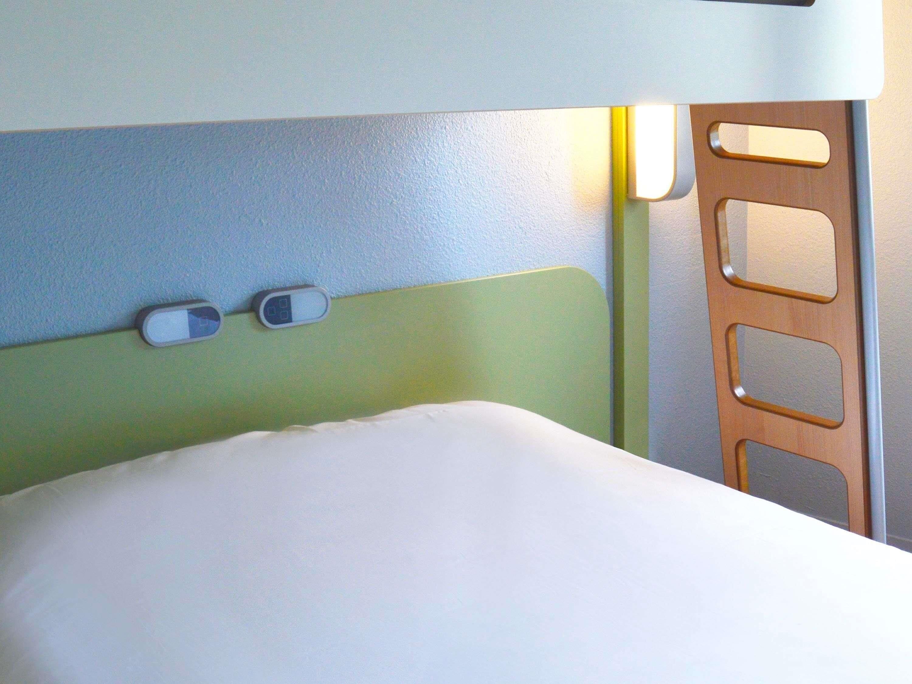 Una cama con colchón blanco y cabecera con interruptor de luz y panel de control.