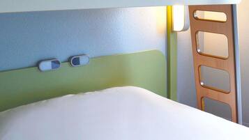 Una cama con colchón blanco y cabecera con interruptor de luz y panel de control.