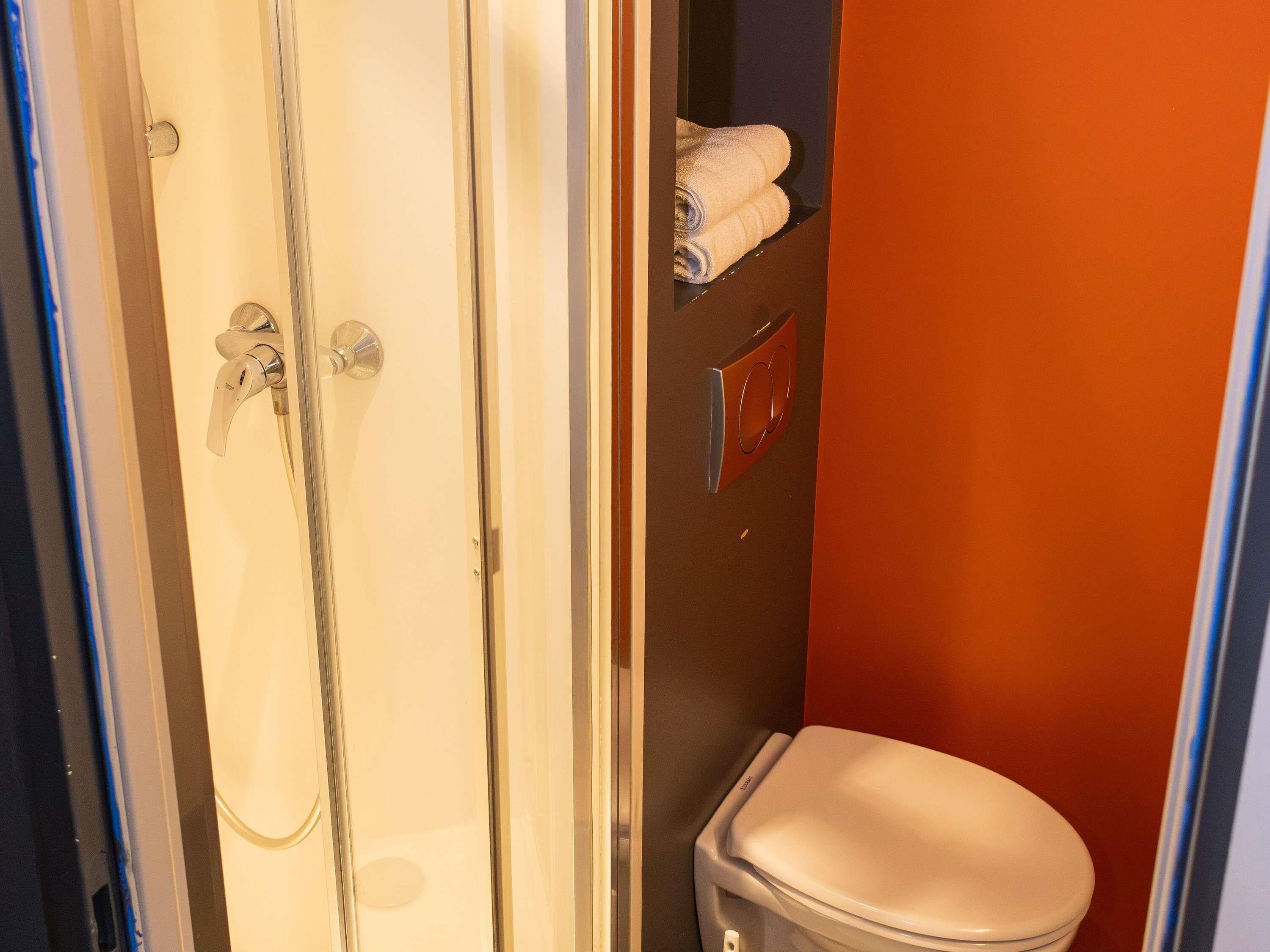 Baño con ducha, inodoro y toallero.