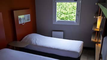 A room with two beds, a window with a view of greenery, a wall-mounted light, and a small table.