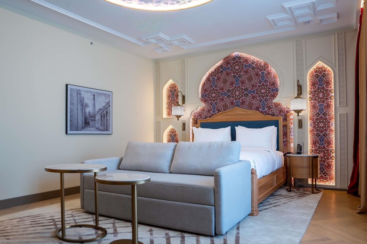 A modern hotel room with a bed, a sofa, a small table, and decorative wall panels.