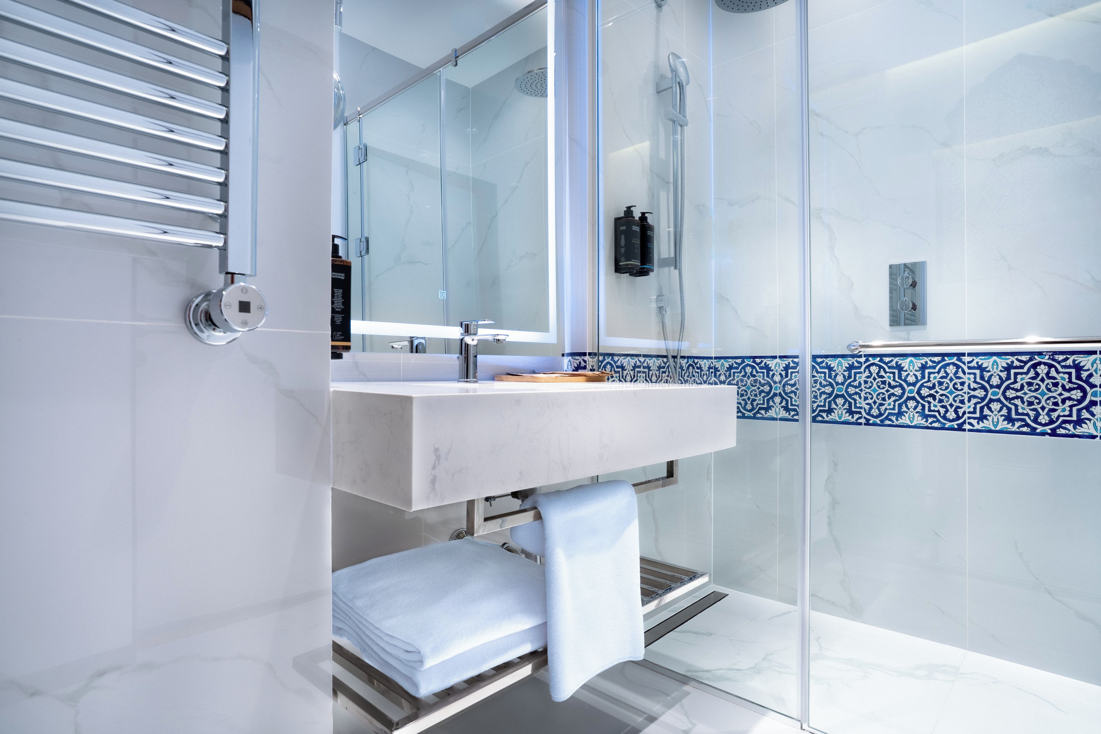 Ein modernes Badezimmer mit einer Duschkabine aus Glas, einem weißen Waschbecken und einer blau-weißen Fliesenfassade.