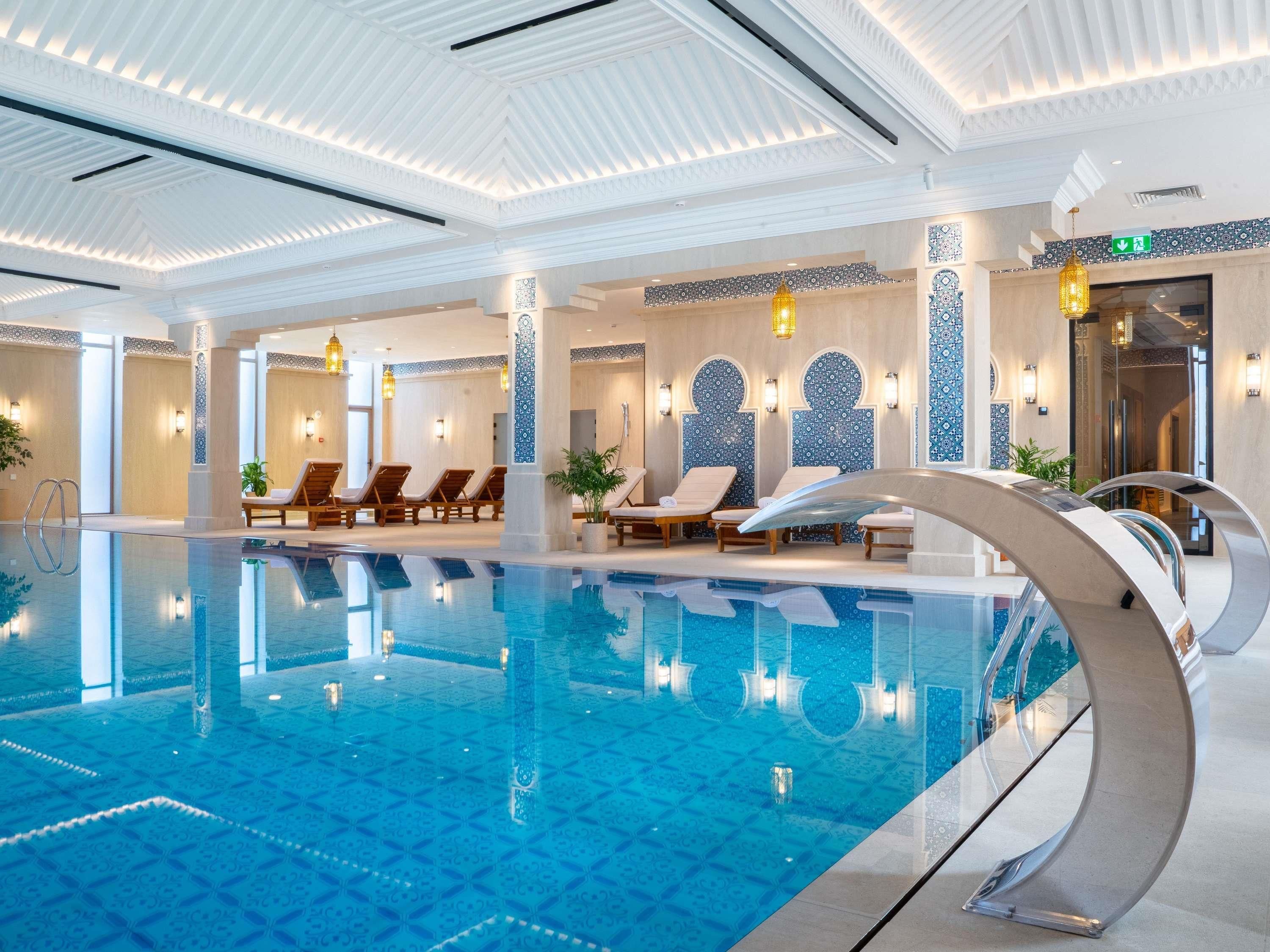 An indoor swimming pool with lounge chairs and decorative wall tiles.