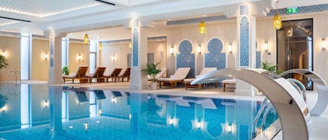 An indoor swimming pool with lounge chairs and decorative wall tiles.