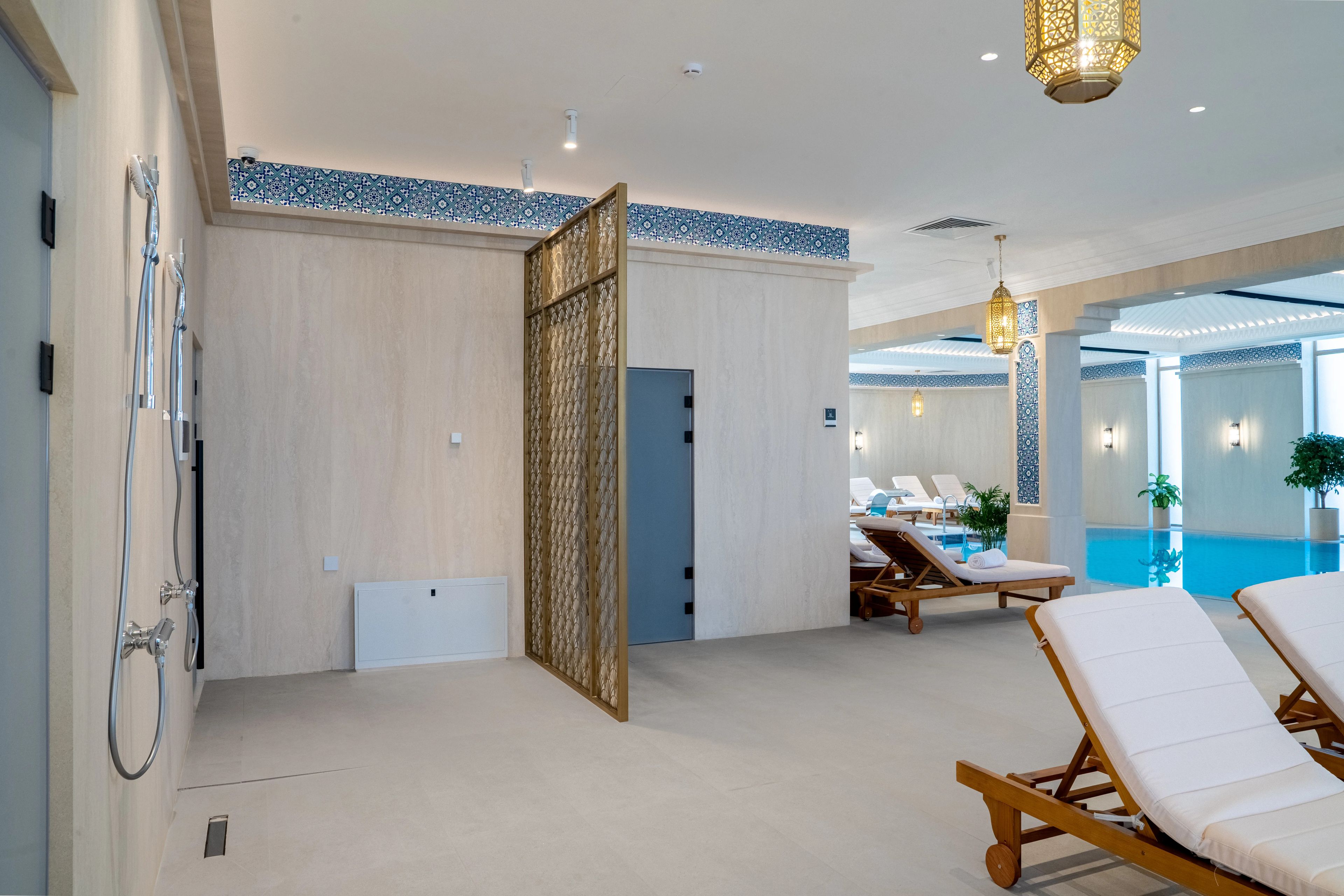 Un área de piscina interior moderna con sillones de descanso, zona de duchas e iluminación decorativa.