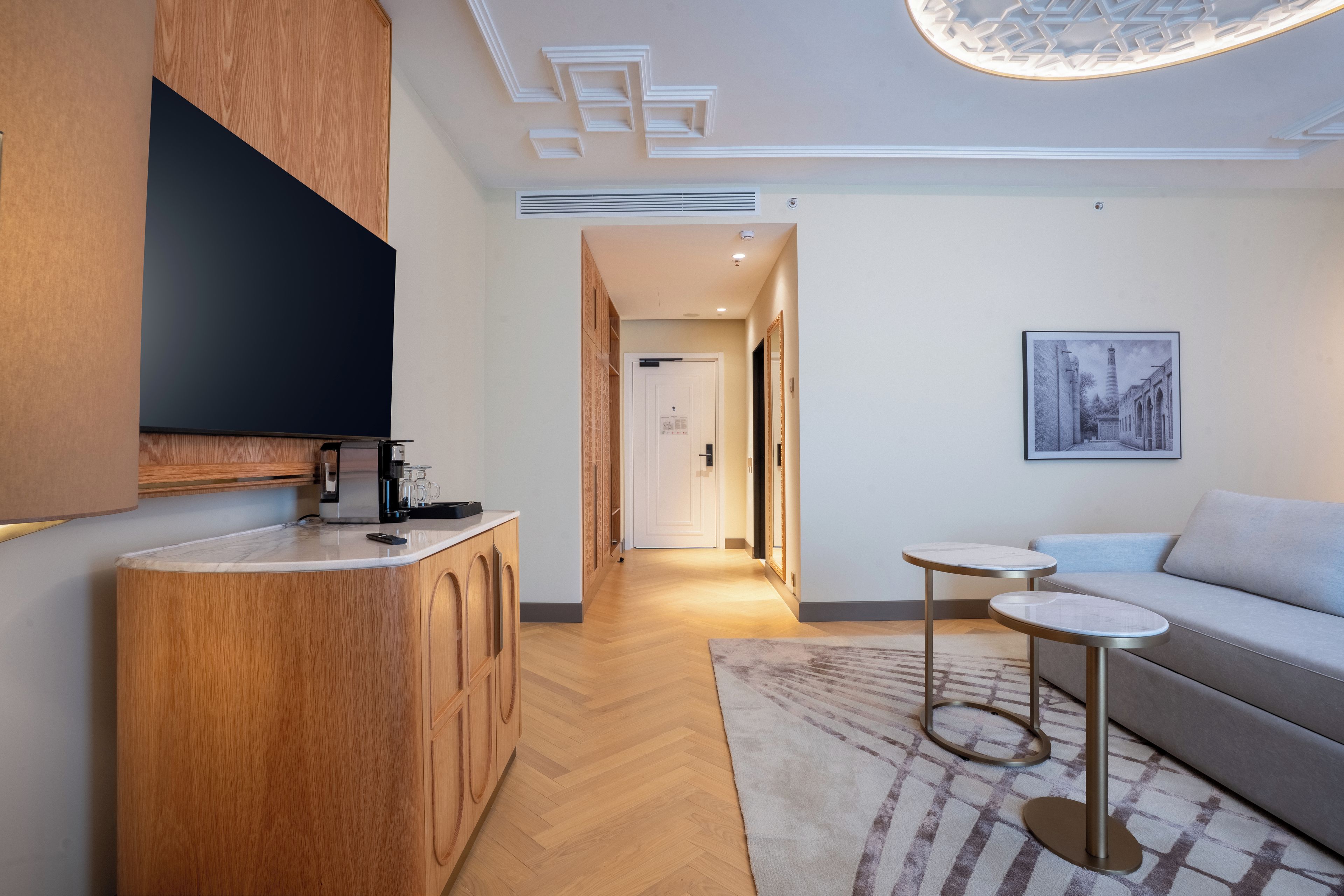 A modern kitchen with wooden cabinets, a flat-screen TV, and a coffee machine.
