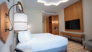 Quarto de hotel com cama, televisão, escrivaninha e guarda-roupa.