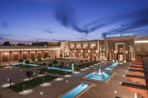 A hotel with a modern facade, multiple entry points, and a well-lit outdoor pool area. - Mercure Khiva (Khiva)