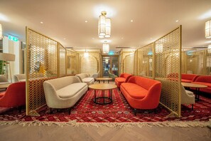 A hotel lobby with a red patterned carpet, beige and red sofas, a small round table, and a decorative partition. - Mercure Khiva (Khiva)