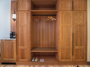 Un armario de madera con una barra para colgar ropa, un par de zapatillas y una cafetera sobre la encimera.