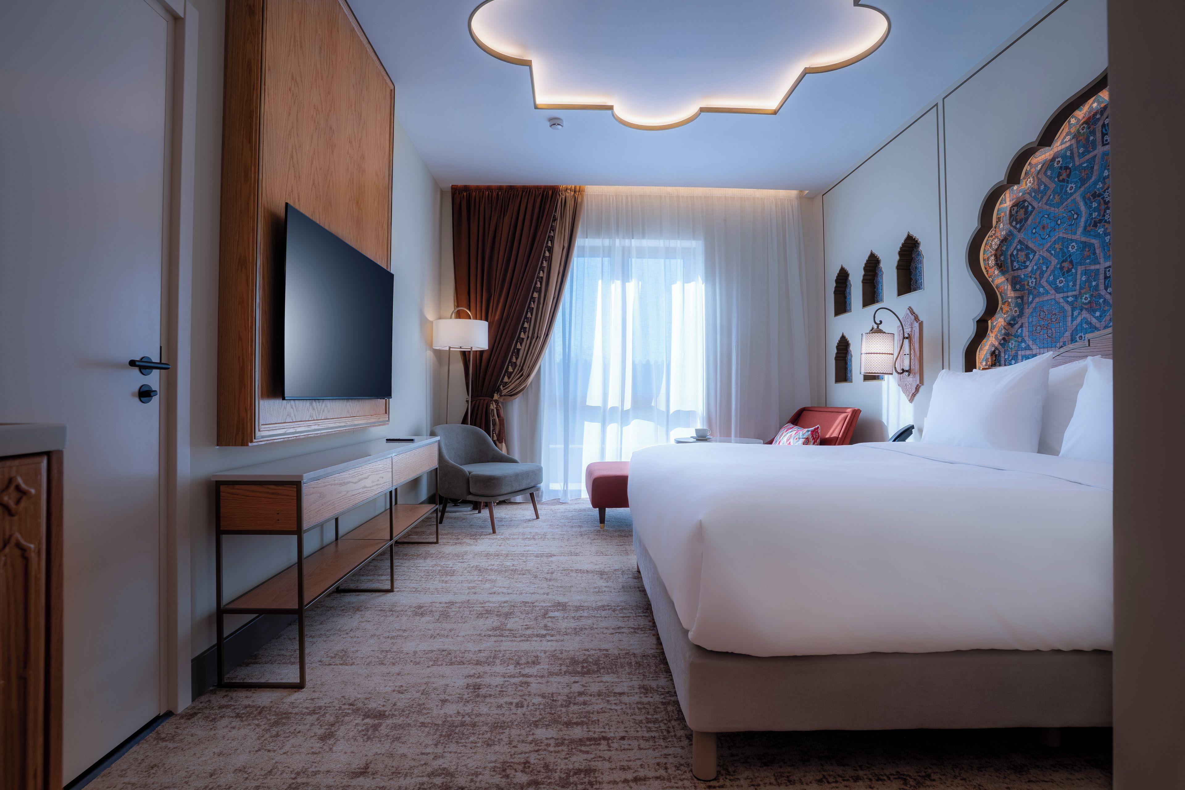 A hotel room with a large bed, a TV, a desk, and a chair.