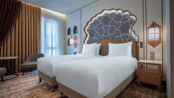 Habitación de hotel con dos camas, una silla, una mesita pequeña y un panel decorativo en la pared.