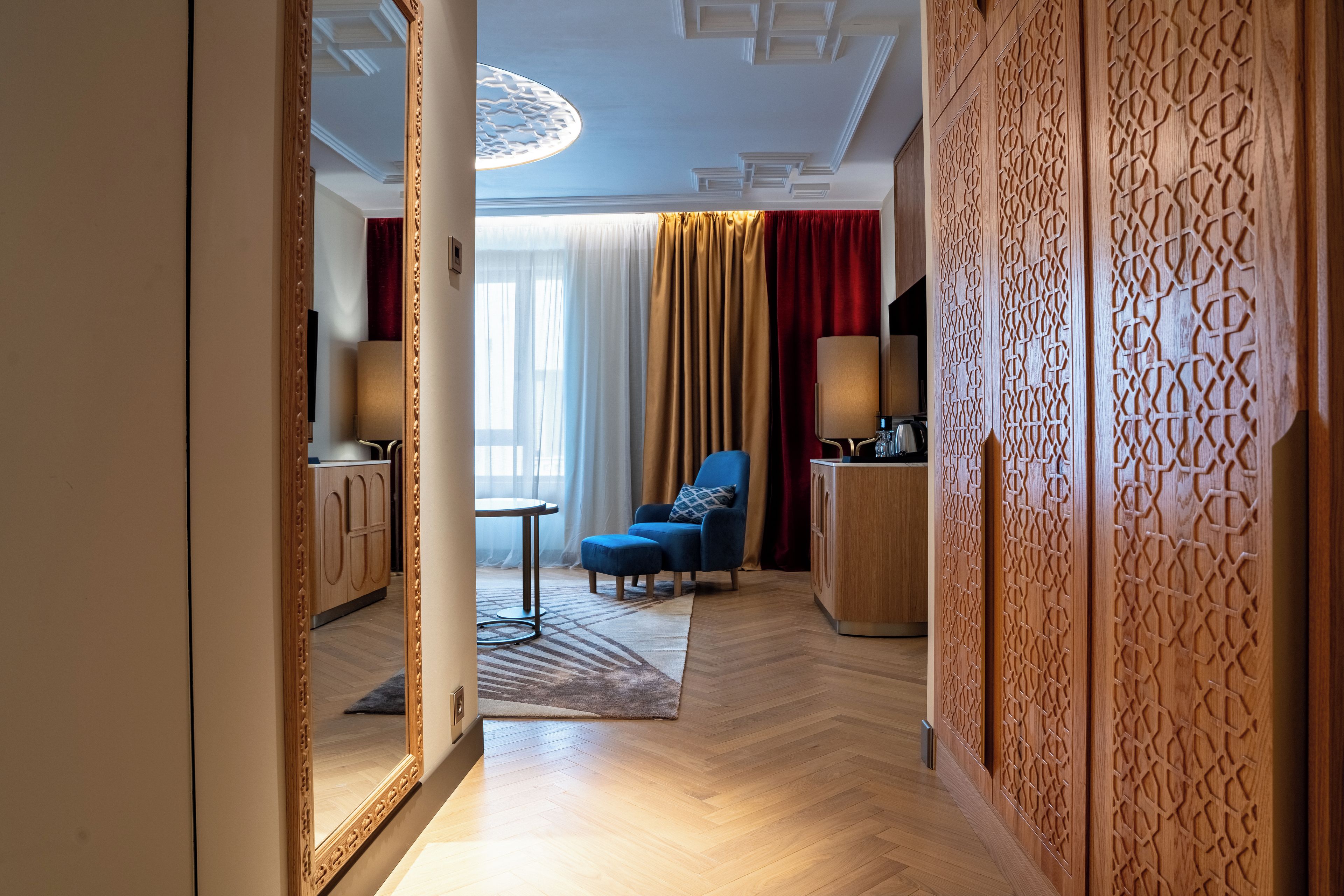 A hotel room with a wooden floor, a blue sofa, a small table, a lamp, and a decorative wall panel.