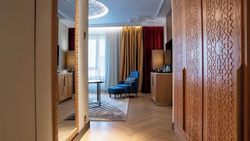 A hotel room with a wooden floor, a blue sofa, a small table, a lamp, and a decorative wall panel.
