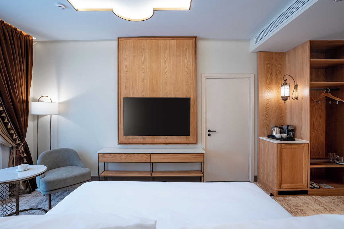 Habitación de hotel con cama, escritorio con televisor de pantalla plana, una silla, armario y mesita de noche con lámpara.