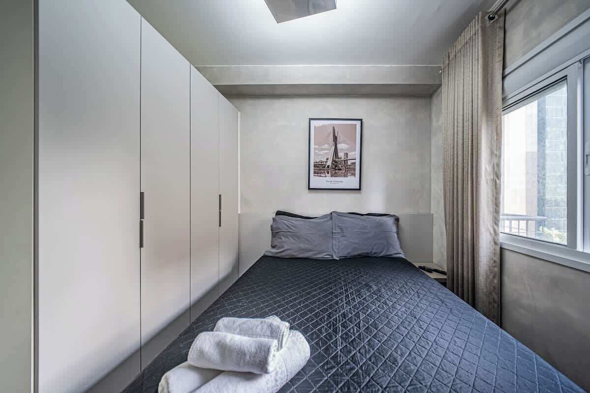 Ein Hotelzimmer mit einem Bett, einem Vorhangfenster, einem gerahmten Bild an der Wand und einem Handtuch auf dem Boden.