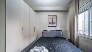 Habitación de hotel con cama, ventana con cortinas, un cuadro en la pared y una toalla en el suelo.