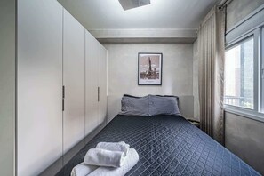 Une chambre d’hôtel avec un lit, une fenêtre avec des rideaux, un tableau encadré au mur et une serviette sur le sol.