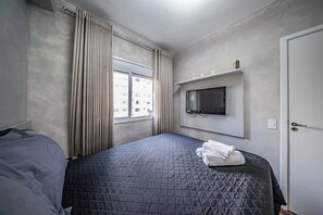 Une chambre d’hôtel avec un lit, un téléviseur fixé au mur, une fenêtre avec des rideaux et une porte.