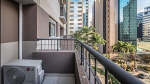 Un balcón con un equipo de aire acondicionado LG, baranda metálica y vista a edificios altos y palmeras.