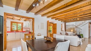 A spacious living area with a wooden dining table, white sofas, and a staircase leading to an upper level. - Private Pool Villa in Pollensa (Pollença)