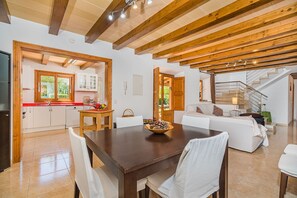 A spacious living area with a wooden dining table, white sofas, and a staircase leading to an upper level. - Private Pool Villa in Pollensa (Pollença)