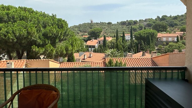 En balkon med udsigt over en landsby på en bakke, en stol og et grønt hegn.
