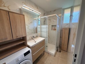 Ein modernes Badezimmer mit Marmor-Spritzschutz, einer Glasdusche und einer integrierten Waschmaschine.