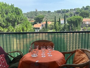 Varanda com mesa posta para quatro pessoas, com vista para uma colina com árvores e edifícios.
